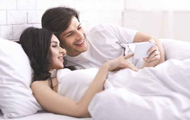 Fiatal házaspár néz fényképeket mobiloddal - Fotó, kép