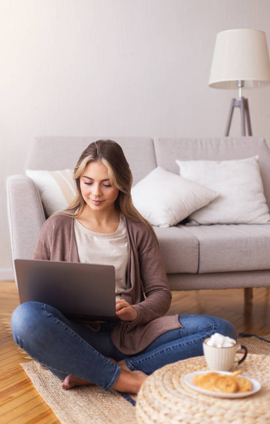 Millennial girl typing on laptop, studying on floor at home - Valokuva, kuva