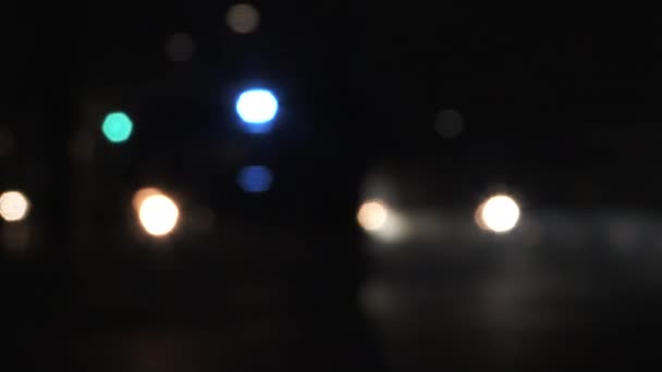 Nierozpoznawalny i niewyraźny ruch drogowy prowadzony przez zaparkowany samochód policyjny z lampkami błyskowymi w nocy. - Materiał filmowy, wideo