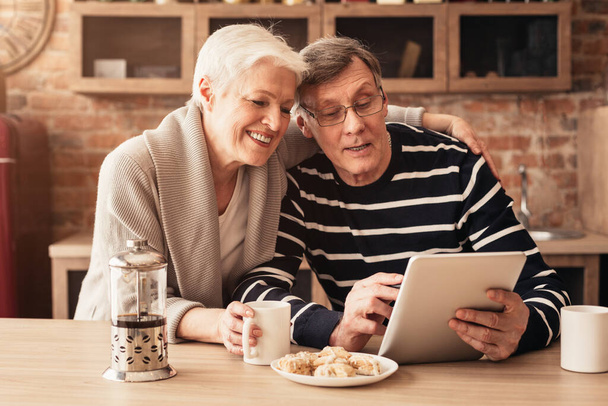 Happy Senior Couple Using Digital Tablet And Drinking Coffee In Kitchen - Fotoğraf, Görsel