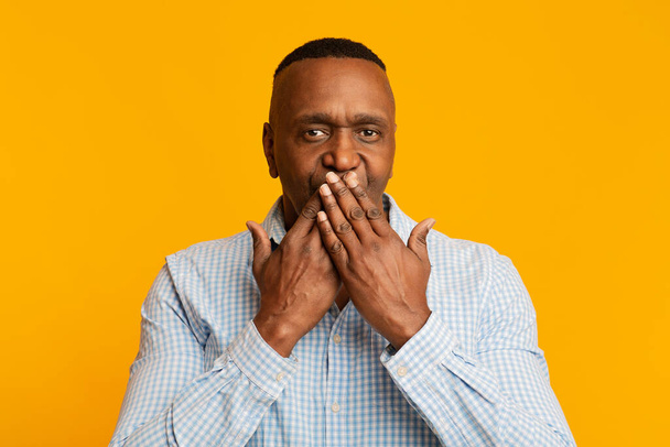 Зрілий африканський чоловік закриває рот, помаранчевий фон
 - Фото, зображення