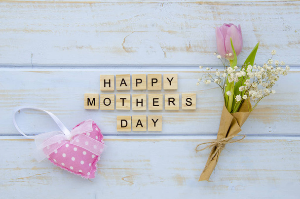 Ξύλινα μπλοκ με γράμματα έκανε σημάδι Happy Mothers Day, που περιβάλλεται από μικρό μπουκέτο με τουλίπα και αισθάνθηκε μαξιλάρι καρδιά. Ξύλινο φόντο, επίπεδη lay - Φωτογραφία, εικόνα