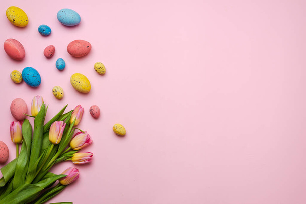 Easter background with colorful eggs and yellow tulips over wood. Top view with copy space - Photo, Image