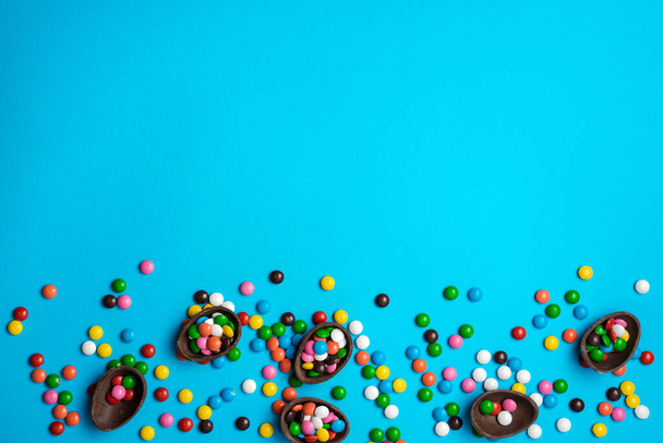 Velikonoční čokoládové vejce s barevnou explozí bonbónů a bonbónů na modrém pozadí. Ležel. Horní pohled - Fotografie, Obrázek