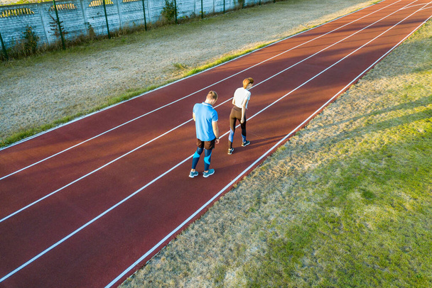 Felülről lefelé légi kilátás két fiatal sportoló és a piros gumi futó pályán egy stadion pihenő után kocogás maraton nyáron. - Fotó, kép