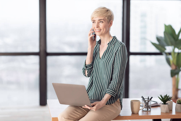Entrepreneur Woman Talking On Cellphone Sitting On Desk In Office - 写真・画像