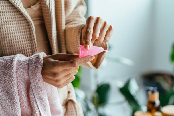 Close-up van de hand van de vrouw opvouwbare menstruatiecup tonen hoe te gebruiken, c vorm. Vrouwen gezondheidsconcept. Hoe menstruatiecup te gebruiken. Vrouwelijke hygiëne, milieuvriendelijk, geen afval, hergebruik concept. - Foto, afbeelding