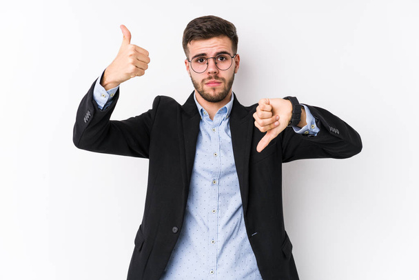 Young caucasian business man posing in a white background isolated Young caucasian business man showing thumbs up and thumbs down, difficult choose concept - Photo, Image