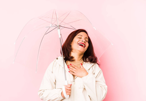 Middle age latin woman wearing an umbrella isolated laughs out loudly keeping hand on chest. - Foto, afbeelding
