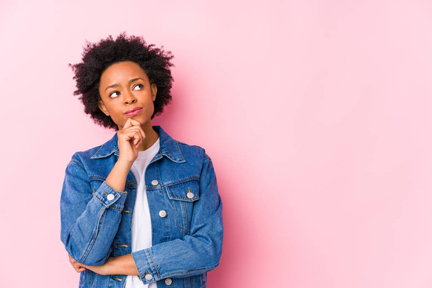Молода афроамериканська жінка проти рожевого фону ізольованого погляду в сторону з сумнівним і скептичним виразом. - Фото, зображення