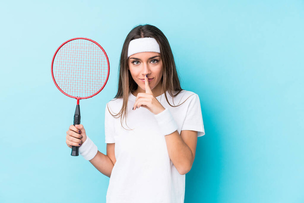 Junge kaukasische Frau spielt Badminton isoliert hält ein Geheimnis oder bittet um Schweigen. - Foto, Bild