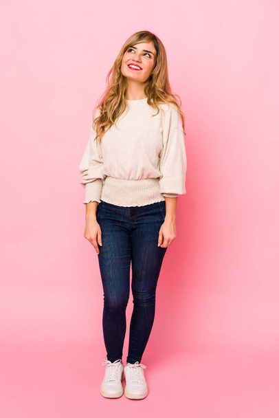 Молодая блондинка-кавказка, стоящая на розовом фоне и мечтающая о достижении целей и целей
 - Фото, изображение