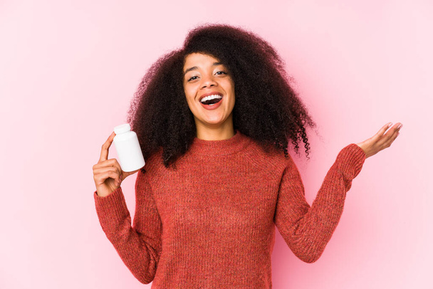 Young afro woman holding a vitamins isolated Young afro woman holding a vitaminsreceiving a pleasant surprise, excited and raising hands. - Fotó, kép