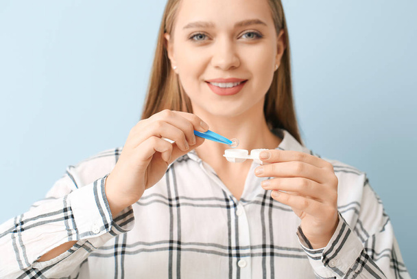Young woman with contact lens case and tweezers on grey background - Valokuva, kuva