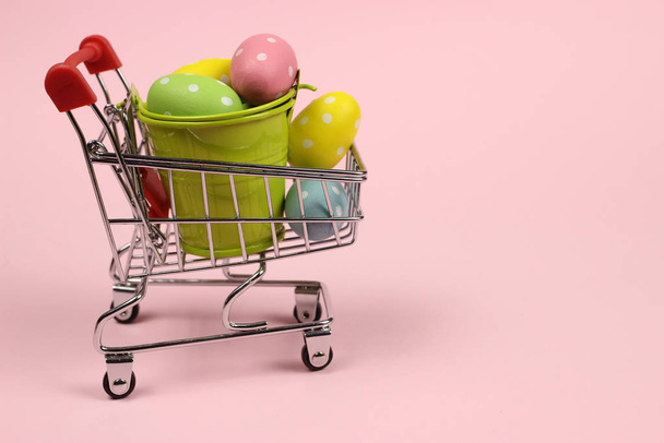 Easter colored eggs in the shopping cart, trolley on a pink background - Photo, image