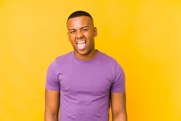Young latin man isolated on yellow background funny and friendly sticking out tongue. - Photo, Image