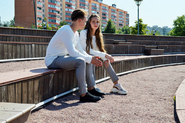 Mladá dívka a mladý muž ve stejném oblečení sedí na dřevěné lavičce - Fotografie, Obrázek