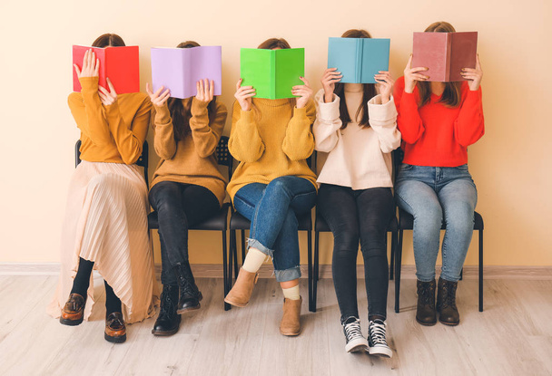 Jonge vrouwen met boeken zitten in de buurt van kleur muur - Foto, afbeelding