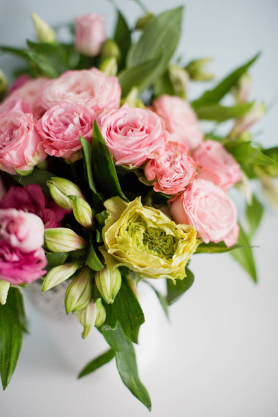 Fényes csokor rózsákkal, eustomával és alstroemériával fehér vázában. Csokor puha kék háttér - Fotó, kép