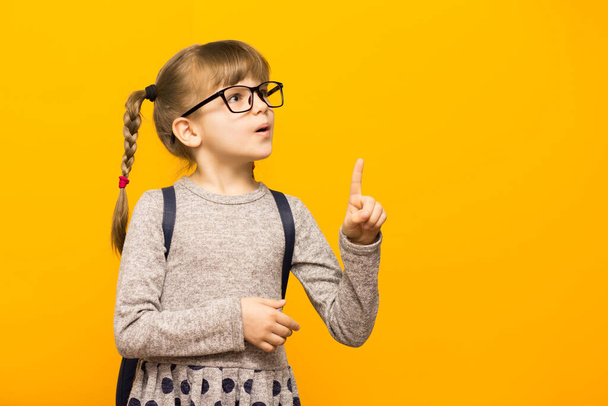Portrait of stylish child girl pointed finger up. Little child in glasses has idea. Kid isolated on yellow background. Success, creative idea concept. - Valokuva, kuva
