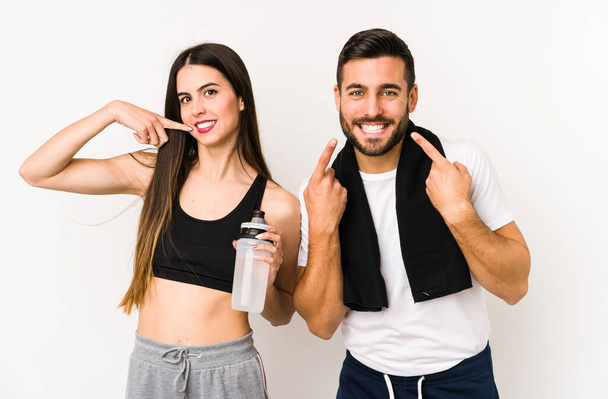 Junge kaukasische Fitness-Paar isoliert lächelt und zeigt mit dem Finger auf den Mund. - Foto, Bild