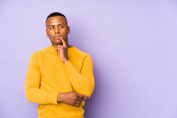 Young latin man isolated on purple background looking sideways with doubtful and skeptical expression. - Foto, afbeelding