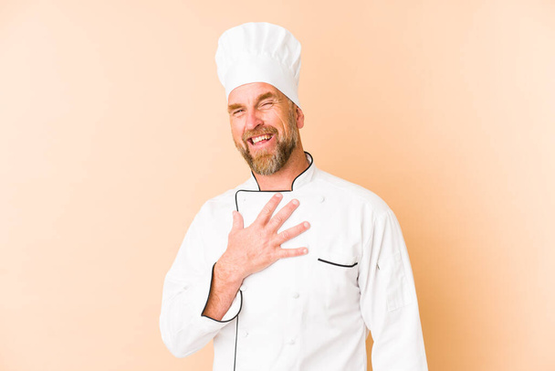 Chef man isolated on beige background laughs out loudly keeping hand on chest. - Photo, Image