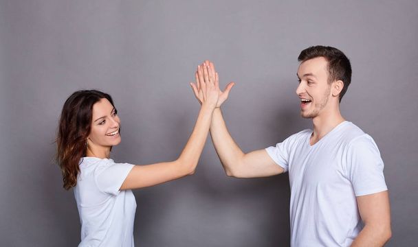 Portrait of Caucasian couple man and woman in basic white t-shirts rejoicing giving high five together isolated on gray background. - Foto, immagini