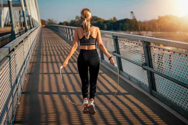 Yetişkin bir fitness kadını köprüde ip atlıyor. Zindelik ve yaşam tarzı kavramı. - Fotoğraf, Görsel