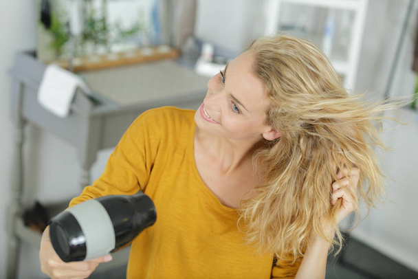 woman dries hair a hair dryer in a bathroom - Φωτογραφία, εικόνα
