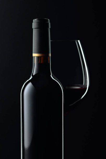 Botella cerrada y copa de vino tinto sobre fondo negro. Copiar espacio
. - Foto, Imagen