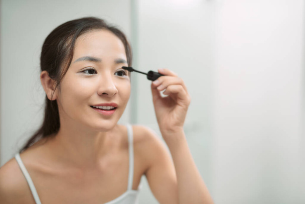 jong aziatische vrouw toepassing mascara in badkamer - Foto, afbeelding