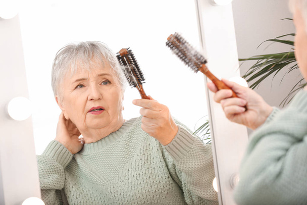 Aynanın yanında saç dökülme sorunu olan yaşlı bir kadın. - Fotoğraf, Görsel