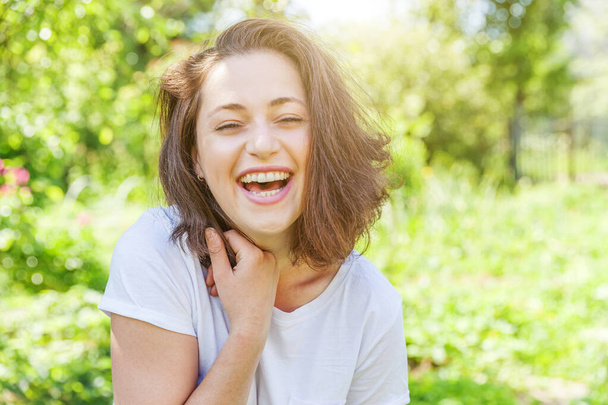 Happy girl smiling outdoor. Beautiful young brunete woman with brown hair resting on park or garden green background. European woman. Positive human emotion facial expression body language - Valokuva, kuva