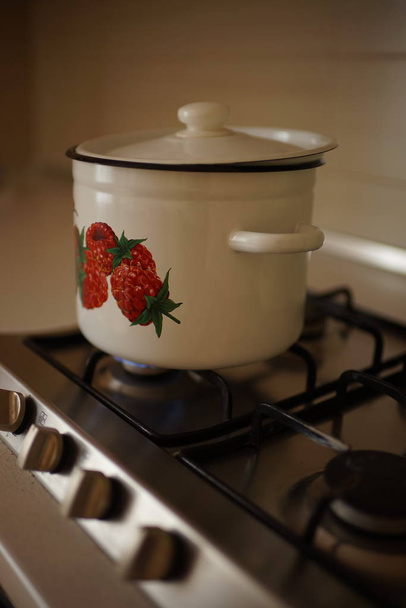 Емалева сковорода з трохи відкритою кришкою під час приготування на газовій плиті
 - Фото, зображення