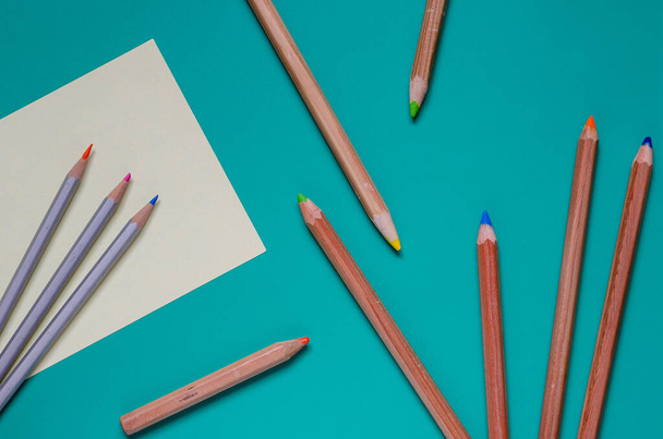 Een groep kleurrijke potloden willekeurig op een turquoise achtergrond. Tien verschillende gebruikte houten potloden. Zicht van bovenaf. Selectieve focus. Close-up. - Foto, afbeelding