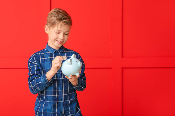 Cute boy putting money in piggy bank on color background - Foto, immagini