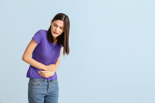 Young woman suffering from menstrual cramps on light background - Photo, Image
