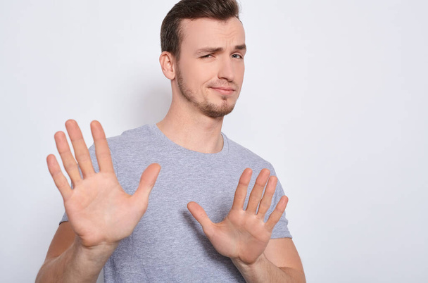 A young handsome white guy in a gray basic T-shirt, stretched his arms forward, shows his hands stop, does not want. The sad man says timeout, stop, shows reluctance. - Foto, Bild