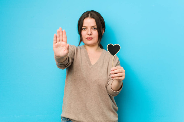 Fiatal plusz méret görbe nő kezében szív alakú álló kinyújtott kézzel mutatja stop jel, megakadályozza, hogy. - Fotó, kép