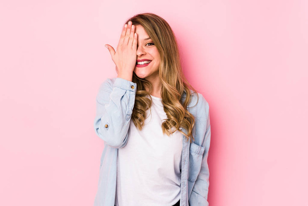 Young caucasian woman isolated on pink background having fun covering half of face with palm. - Valokuva, kuva