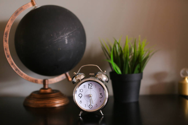 Черный монохромный глобус и часы, стоящие на столе рядом с комнатным стеклом
. - Фото, изображение