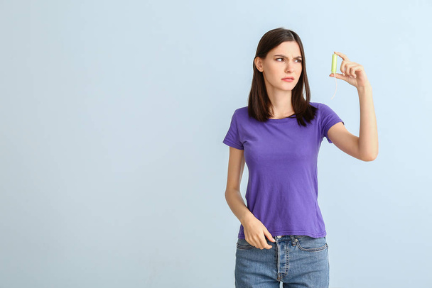 Troubled woman with menstrual tampon on light background - Foto, afbeelding