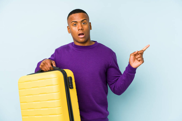 Mladý cestovatel muž drží kufr izolovaný ukazuje do strany - Fotografie, Obrázek