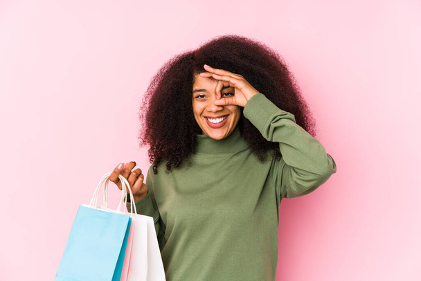 Fiatal afro nő vásárlás elszigetelt Fiatal afro nő vásárol izolaythe nő gazdaság egy rózsa elszigetelt izgatott tartása rendben gesztus a szem - Fotó, kép