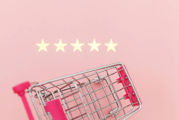 ホイールと5つ星評価でショッピングおもちゃのための小さなスーパーマーケットの食料品プッシュカートは、パステルピンクの背景に隔離されました。小売消費者オンライン評価とレビューの概念を購入 - 写真・画像
