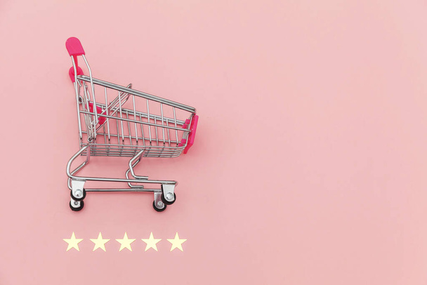 Pequeño supermercado carrito de compras empuje para juguete de compras con ruedas y clasificación de 5 estrellas aislado sobre fondo rosa pastel. Compras al por menor concepto de evaluación y revisión en línea
 - Foto, imagen