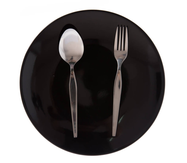 черная керамическая тарелка с алюминиевой вилкой и ложкой изолированы на белом фоне
 - Фото, изображение