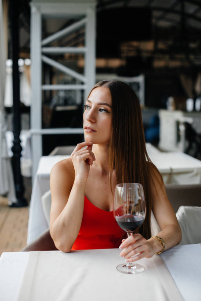 Beautiful young girl sits and drinks wine on the veranda of a beautiful house. Holiday. - Foto, Imagem