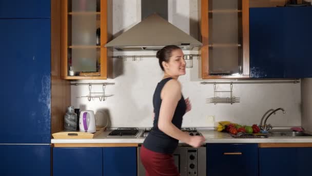 cheerful girl dances and sings having fun in home kitchen - Filmati, video